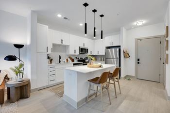 A white kitchen with a white counter top and a stainless steel refrigerator